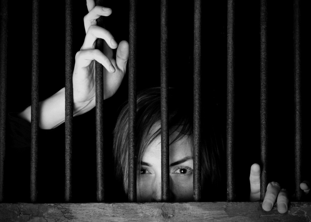 A woman peeking out between the bars of a prison cell - much like the experience of being trapped by bad business advice.