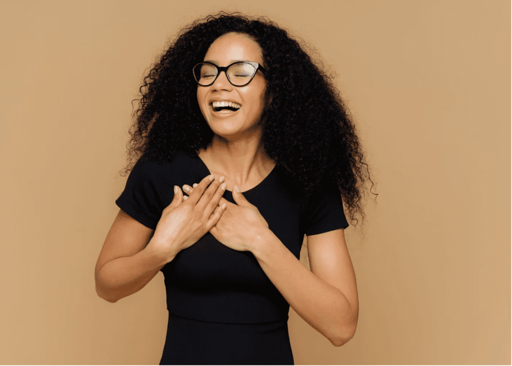 Light skinned black woman with her hands crossed over her heart smiling because she knows gratitude helps achieve your dreams.